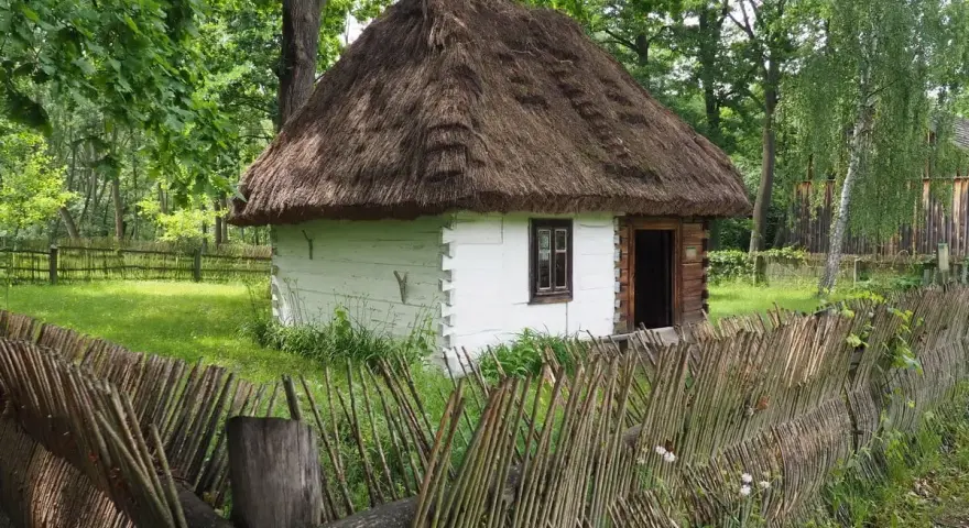 Drewniana chata z krytym strzechą dachem i płotem z gałęzi. Wspaniałe radom atrakcje, które przenoszą w przeszłość.