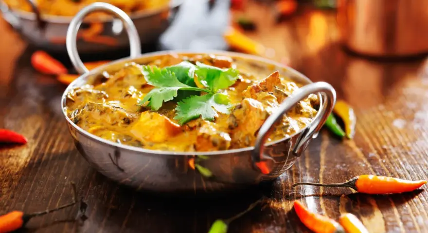 Ein cremiges Curry, garniert mit Koriander, umgeben von bunten Chilis. Ein Genuss für Liebhaber indischer Gerichte.