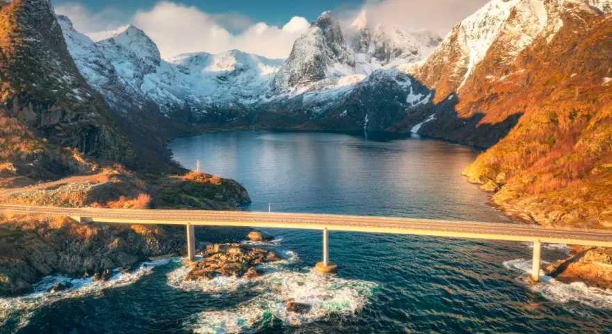 Mosty łączące wyspy w fiordach Norwegii, z ośnieżonymi górami w tle.