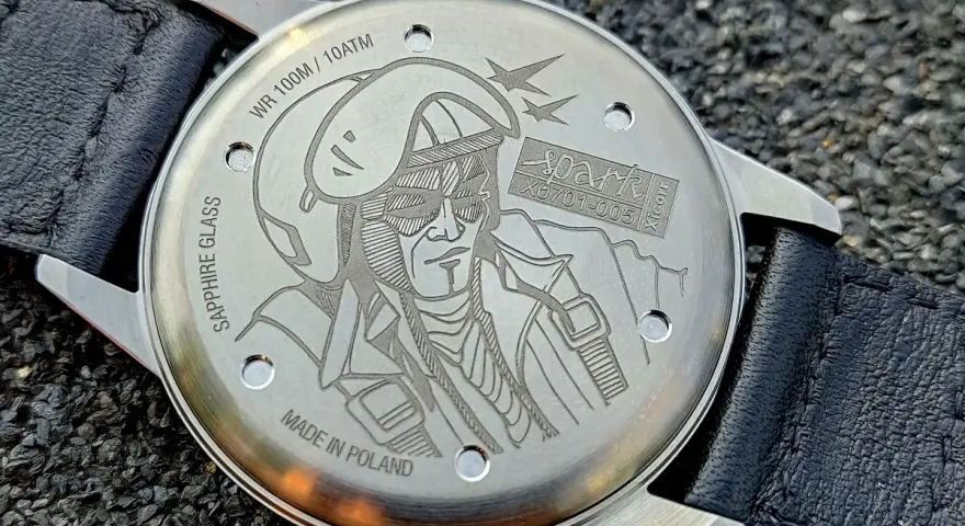 Napis na deklu zegarka: "MADE IN POLAND", WR 100M/10ATM, SAPPHIRE GLASS. Grawer przedstawia pilota w hełmie i goglach.