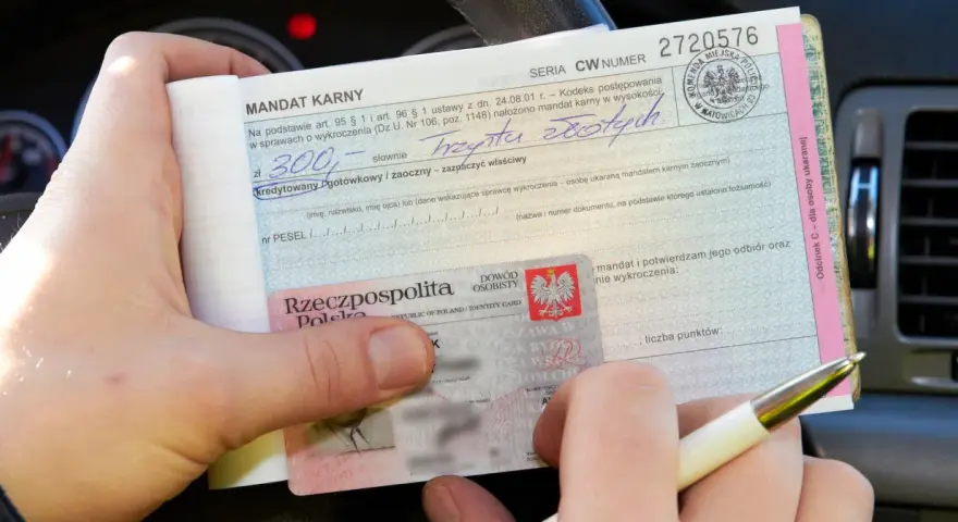 Ręka trzyma mandat karny na kwotę 300 zł, obok dowód osobisty. To kara za wykroczenie, być może związane z parkowaniem.