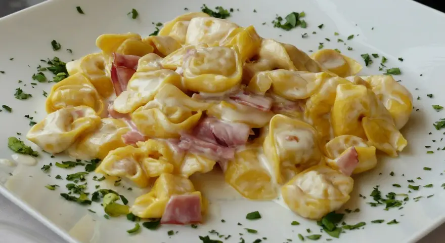 Tortellini panna e prosciutto, un piatto cremoso e saporito, guarnito con prezzemolo fresco su un piatto bianco.