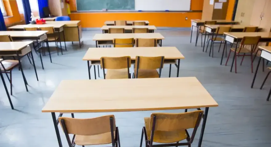 Pusta klasa szkolna z rzędami ławek i krzeseł. W tle tablica i okna. Obowiązek nauki czeka na uczniów.