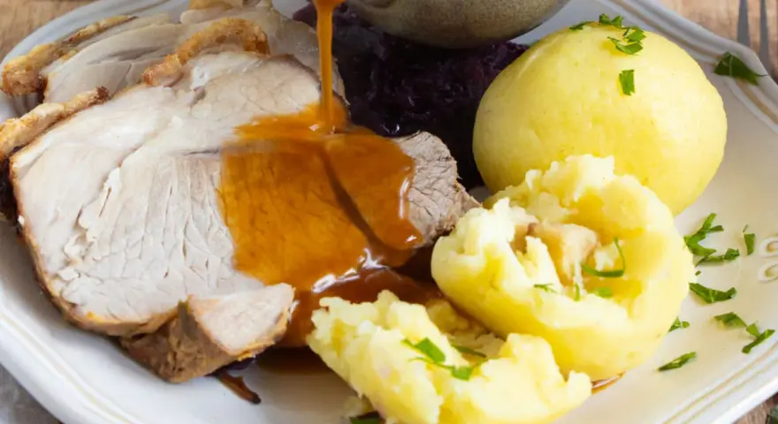 Omas Sonntagsessen: Saftiger Schweinebraten mit knuspriger Kruste, Klößen und Rotkohl, übergossen mit dunkler Soße.