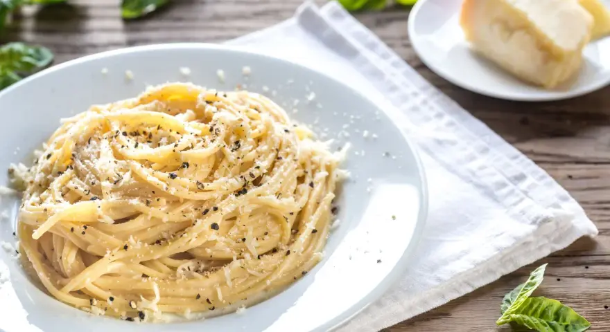 Piatto di pici cacio e pepe, conditi con abbondante pecorino e pepe nero macinato fresco, su un tavolo di legno rustico.