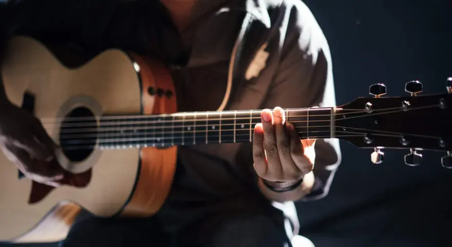 Gitarrist übt den **palm mute**-Effekt auf einer Akustikgitarre, die Finger liegen auf den Saiten.