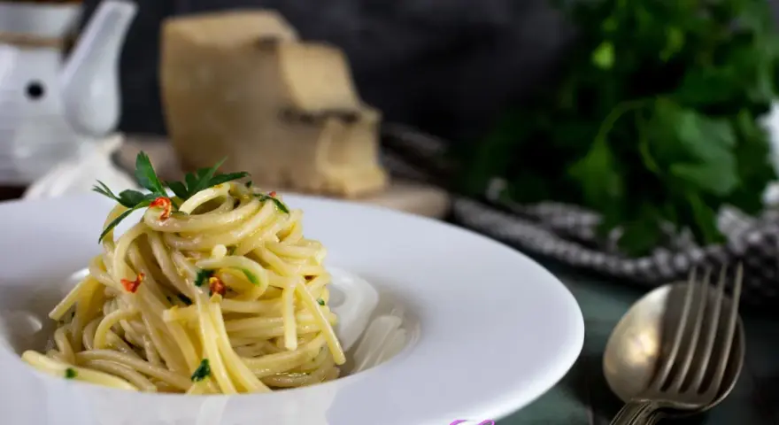 Un piatto di spaghetti alla carrettiera, conditi con aglio, olio, peperoncino e prezzemolo, con pecorino grattugiato sullo sfondo.