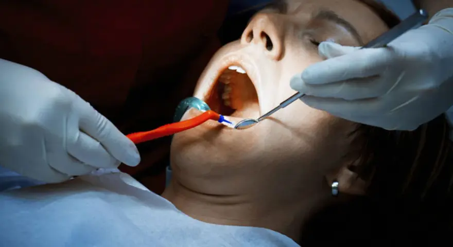 Dentysta bada usta pacjentki, która cierpi na ropień zęba. Widoczne narzędzia stomatologiczne i rozwierak.