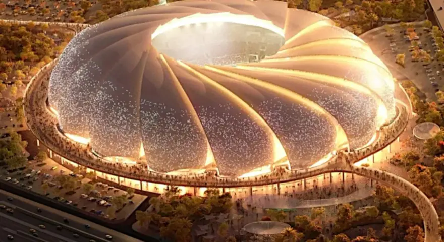 Futurystyczny stadion, który może być najładniejszy na świecie, z falującym dachem i oświetlonymi detalami, otoczony zielenią i tłumem ludzi.
