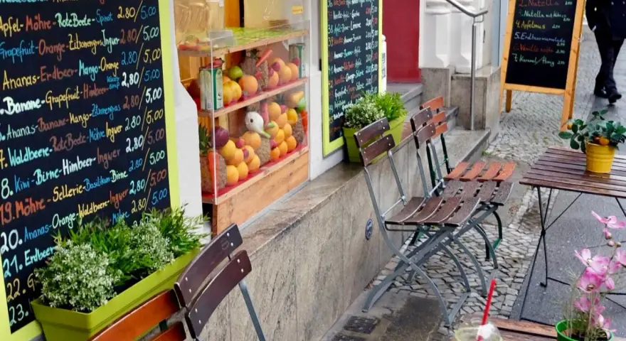 Frischer Smoothie in Berlin. Bunte Tafel mit Frucht- und Gemüsesorten, daneben leere Stühle und ein Tisch.