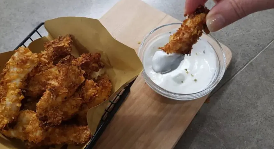 Bocconcini di pollo in friggitrice ad aria, croccanti e dorati, pronti per essere intinti in una salsa cremosa.