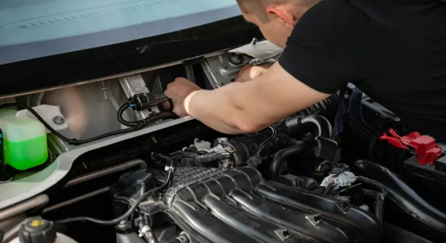 Mechanik naprawia silnik, prawdopodobnie usuwając uciążliwy błąd P0011. Widać zbiornik płynu i elementy silnika.