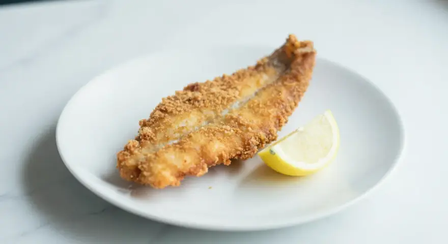 Chrupiący dorsz z airfryer na białym talerzu, z plasterkiem cytryny. Idealny obiad.
