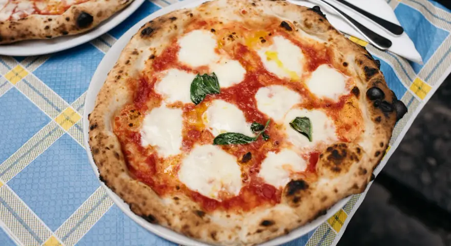 Pyszna pizza napolitana z pomidorami, mozzarellą i bazylią na niebieskim obrusie.
