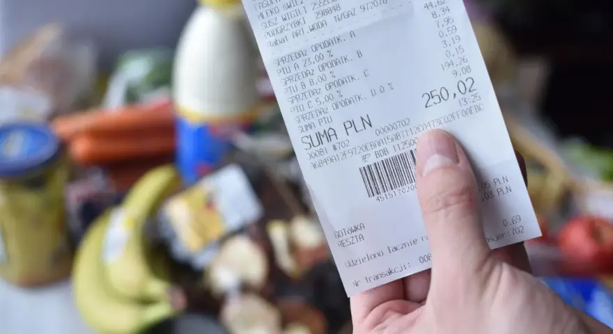 Ręka trzyma paragon z zakupów spożywczych, na którym widnieje suma 250,02 zł. Zastanawiasz się, gdzie wyrzucać paragony? Ten jest z papieru termicznego.