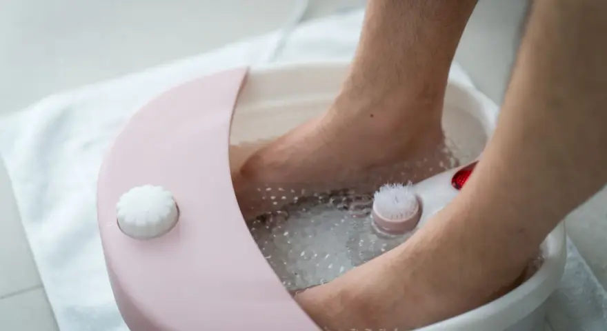 A person's feet are soaking in a foot spa machine filled with bubbly water. You can put water, bath salts, or essential oils in a foot spa machine for a relaxing experience.