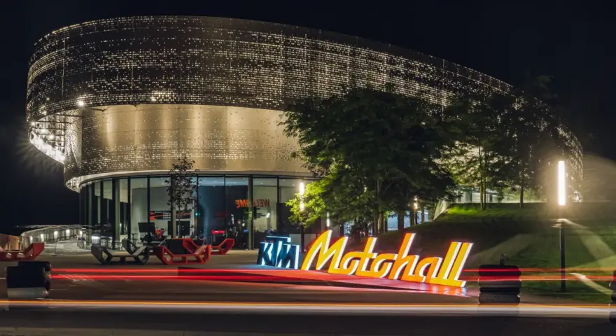 Insegna luminosa KTM Motohall di notte, con il moderno edificio illuminato e le scie luminose delle auto.