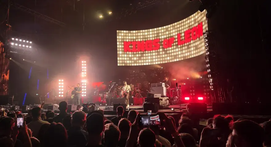 Koncert Kings of Leon na żywo. W tle wielki ekran z napisem "KINGS OF LEON", na scenie zespół gra dla rozentuzjazmowanej publiczności.