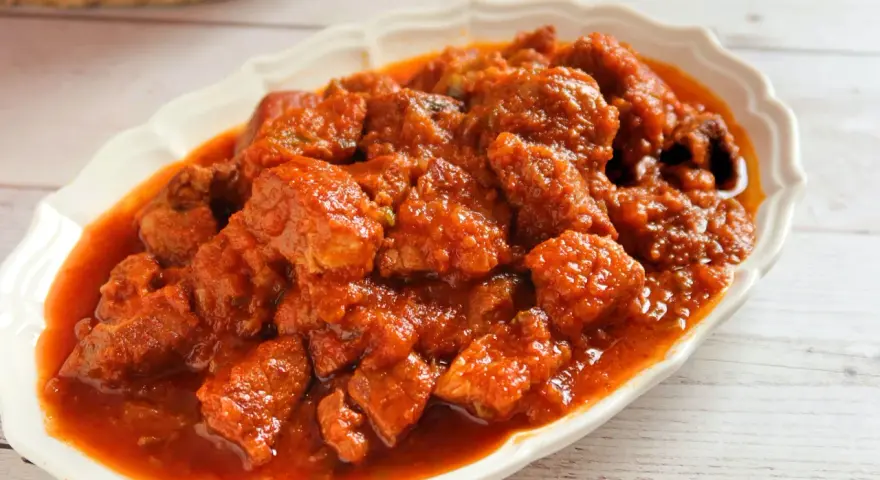 Plato de magro con tomate, trozos de carne tierna en una salsa roja y sabrosa, servido en una fuente blanca.