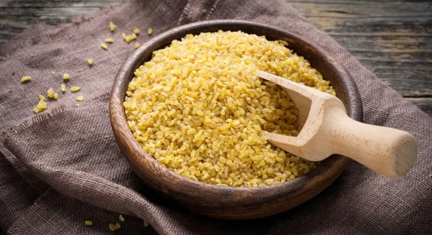 Holzschale mit Bulgur, bereit zum Bulgur kochen. Ein Holzschöpfer liegt darin.