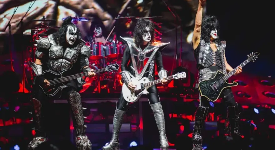 Les membres du groupe de rock Kiss, maquillés et costumés, jouent sur scène. Un chanteur lève un bras en signe de victoire.