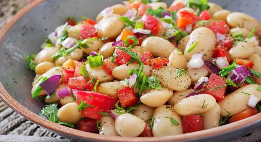 Un'insalata di fagioli sfiziosa, ricca di pomodori freschi, cipolla rossa e erbe aromatiche, servita in una ciotola rustica.