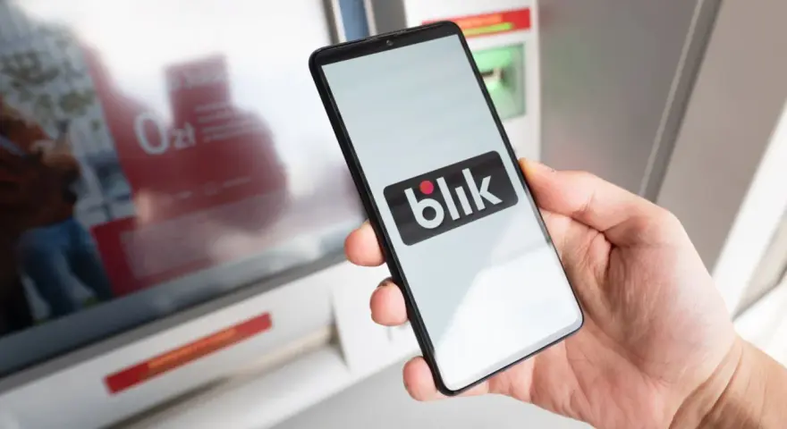Dłoń trzyma smartfon z logo Blik. Czy Blik jest tylko w Polsce? Płatność zbliżeniowa przy bankomacie.