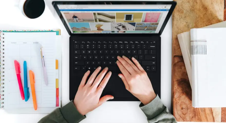 Hände tippen auf einem Laptop, daneben ein Kalender und eine Kaffeetasse.