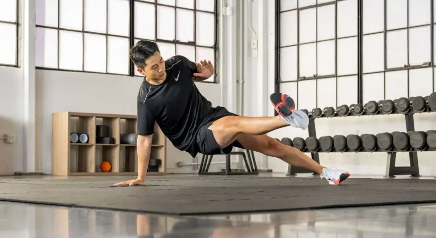 Un homme en tenue de sport exécute un exercice de planche latérale dans une salle de sport.