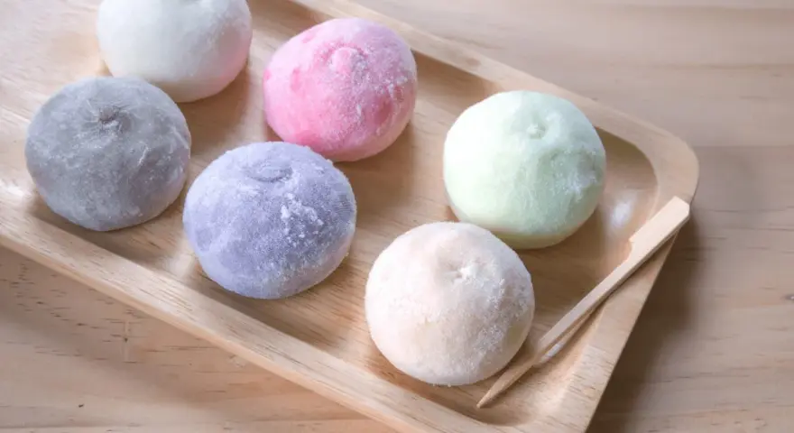 Kolorowe desery azjatyckie, mochi, ułożone na drewnianej tacy.