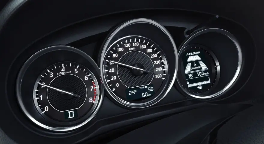 Zbliżenie na deskę rozdzielczą samochodu: obrotomierz pokazuje ok. 1500 obr./min, prędkościomierz ok. 60 km/h, a wyświetlacz i-ELOOP informuje o ładowaniu.