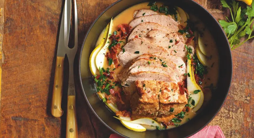 Lonza di maiale in padella morbida, affettata e servita con pere, salsa cremosa e prezzemolo tritato.