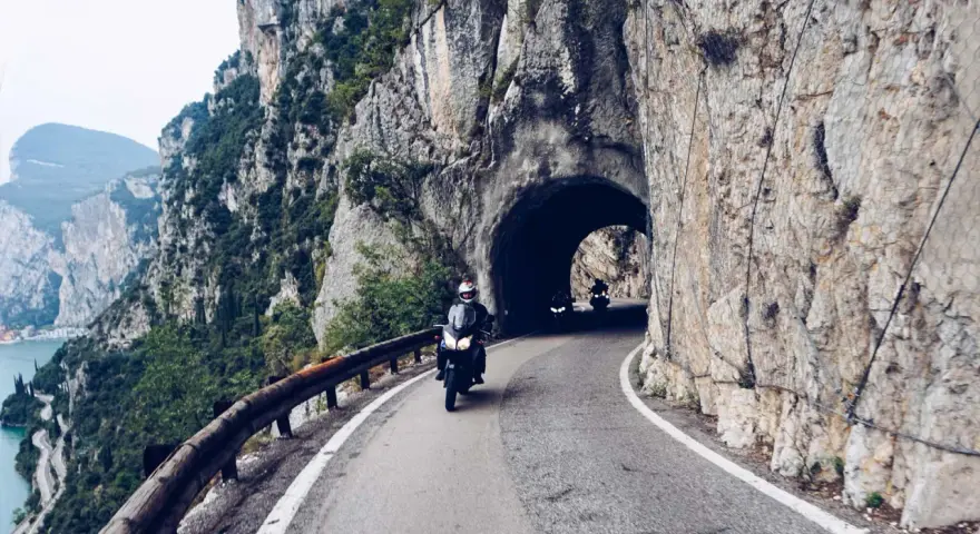 Motocykliści przemierzają malowniczą strada della forra, wjeżdżając w skalny tunel. Widok na jezioro i góry zapiera dech.