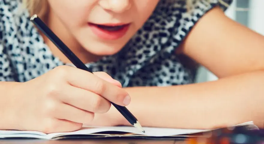Dziecko zmagające się z pisaniem, co może być oznaką dysleksji. Skupienie na twarzy i ręce trzymającej ołówek.