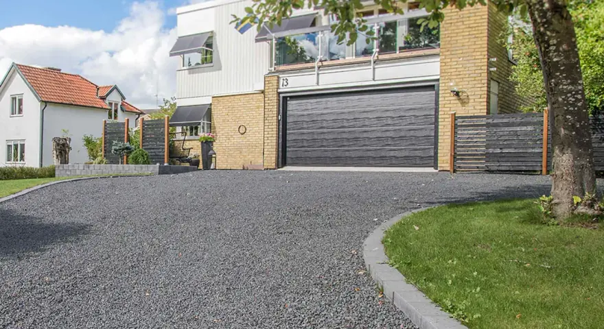 En vacker uppfart med mörkt grus leder fram till ett modernt hus med garageport.