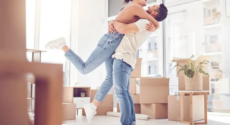 Glückliches Paar umarmt sich in einem neuen Zuhause voller Umzugskartons. Ein aufregender Moment, wann zusammenziehen!