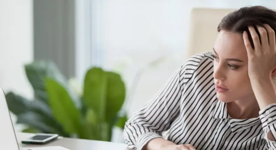 En kvinna sitter vid ett skrivbord, ser ut att vara omotiverad på jobbet. Hon vilar huvudet i handen och tittar tomt framför sig.