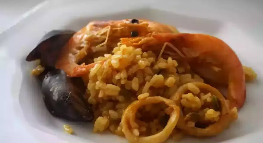 Arroz meloso con langostinos, mejillones y calamares en un plato blanco.