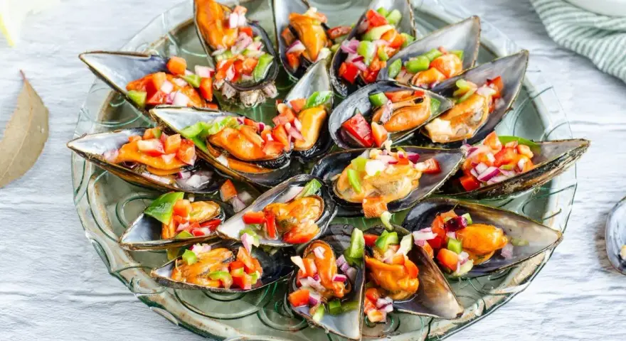 Mejillones a la vinagreta, frescos y coloridos, servidos en su concha con una picada de pimientos y cebolla.