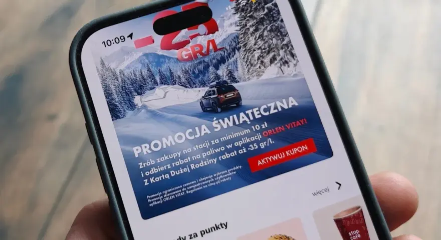 Aplikacja ORLEN z promocją na paliwo za punkty. Zima, góry i samochód na ekranie telefonu.