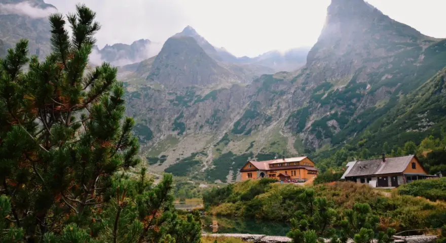 Malownicze tatry słowackie z górami w chmurach, jeziorem i schroniskami.