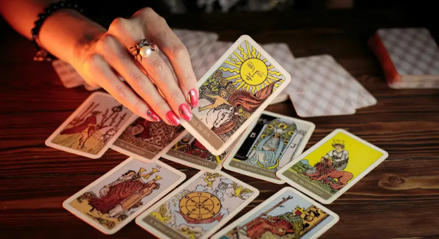 Dłoń z pierścionkiem wybiera kartę Słońce z talii tarot. Rozłożony krzyż celtycki tarot zapowiada przyszłość.