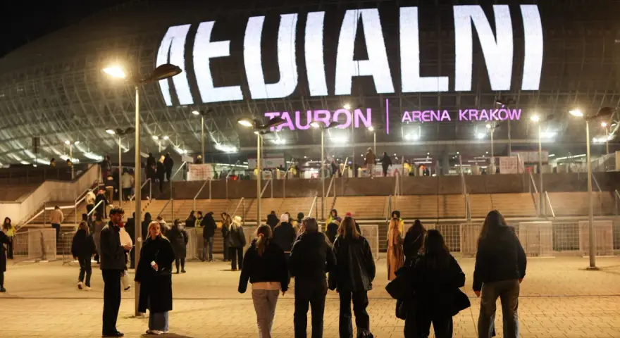 Tłum ludzi zmierza do Tauron Areny Kraków na koncert. Wielki napis na dachu obiektu zapowiada wydarzenie. To prawdziwy **rush w Polsce**!