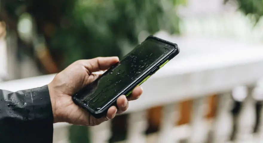 Dłoń trzyma mokry smartfon. IPX4 co oznacza? Ochronę przed zachlapaniem, idealny na deszcz.