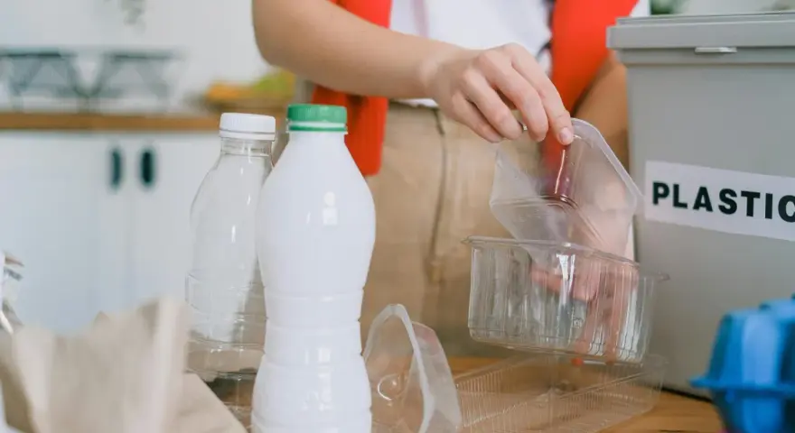 Segregacja odpadów to pierwszy krok, jak ograniczyć plastik. Ręka wrzuca plastikowe opakowania do pojemnika z napisem "PLASTIC".