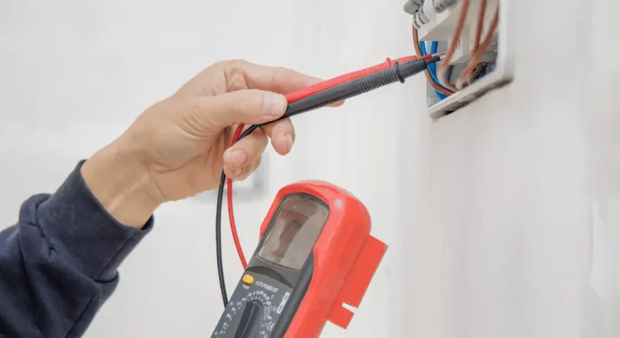 Elektryk sprawdza instalację elektryczną multimetrem, przygotowując protokół odbioru.