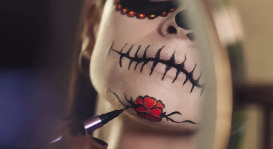 Nahaufnahme eines Gesichts mit Totenkopf-Make-up, das mit einem Pinsel bemalt wird.