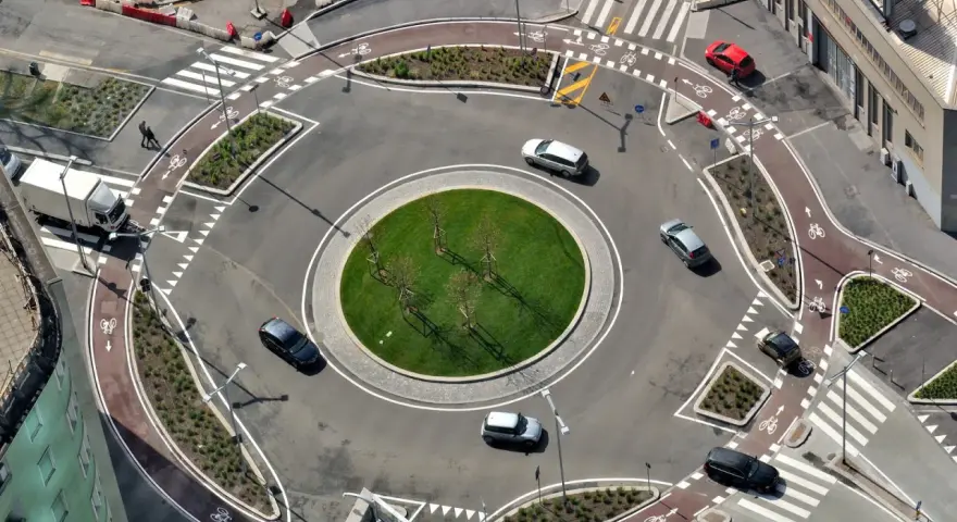 Rotonda con piste ciclabili e segnaletica orizzontale che rispetta l'art. 36 CDS. Auto e camion circolano in un contesto urbano moderno.