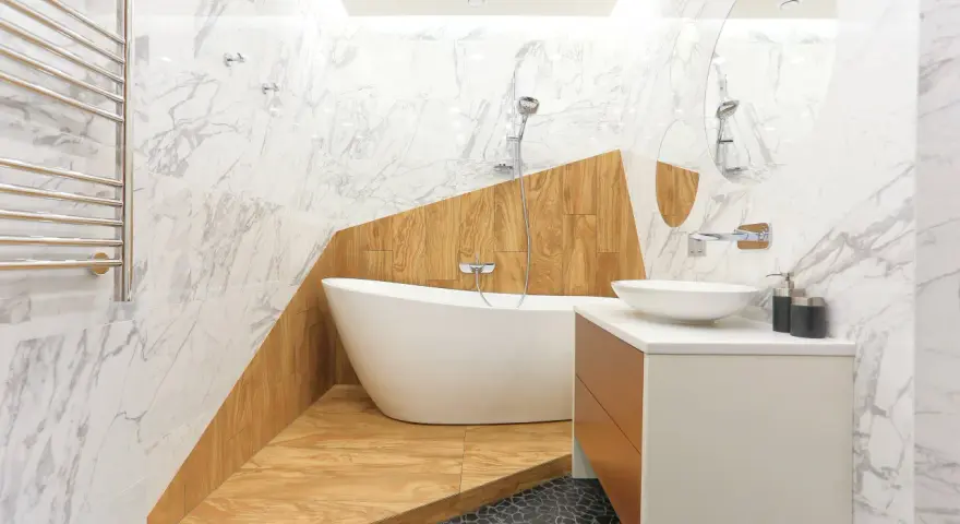 Salle de bain moderne avec baignoire îlot sur une estrade en bois, lavabo, miroir et carrelage marbre.