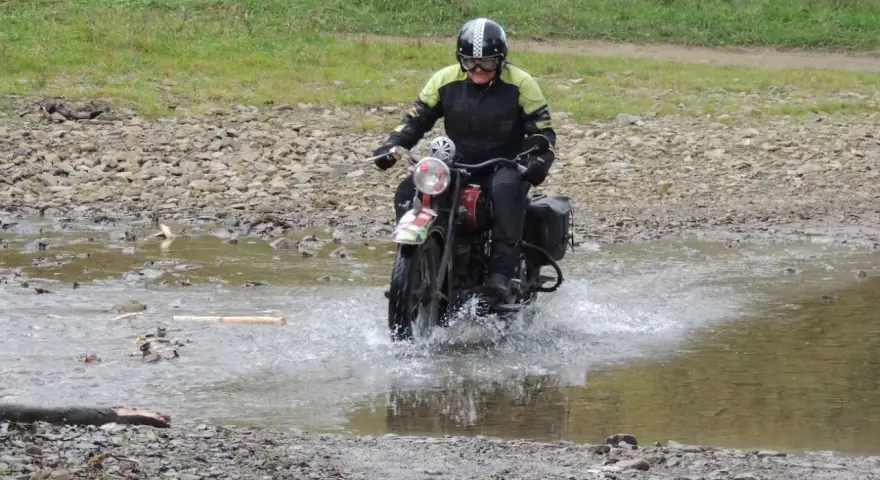 Motocyklista w kasku pokonuje wodną przeszkodę na kamienistej trasie w okolicach Jasła.